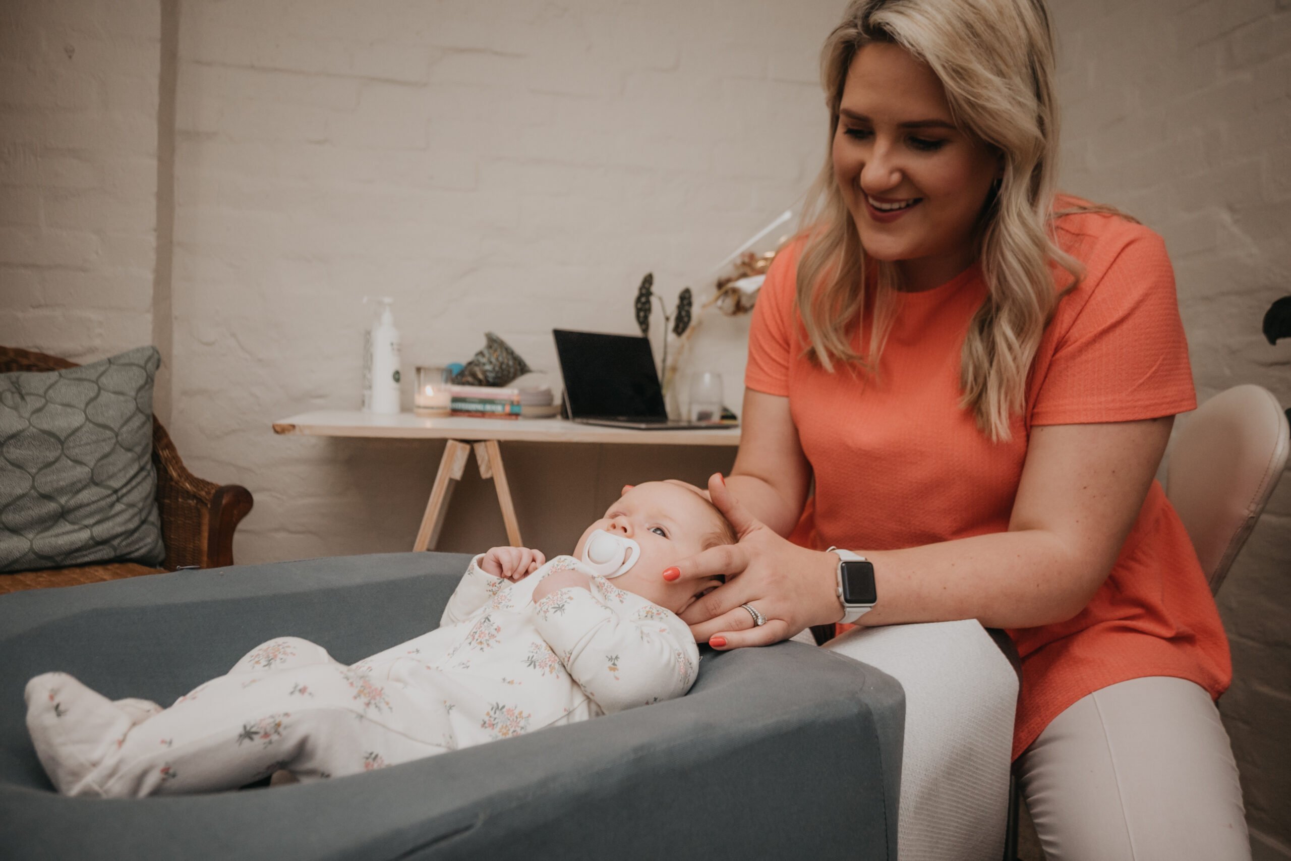 Female chiropractor gently adjusting a baby on a treatment table, with the baby smiling and looking comfortable.